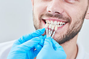 dental veneers TX dentist holding up dental veneers to patient's teeth during dental veneer services tx