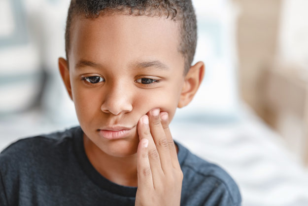 young boy holding his cheek wondering How Does Tooth Decay Develop
