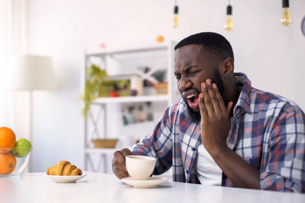 common dental problems man holding his mouth in pain from Common Dental Problems after drinking coffee