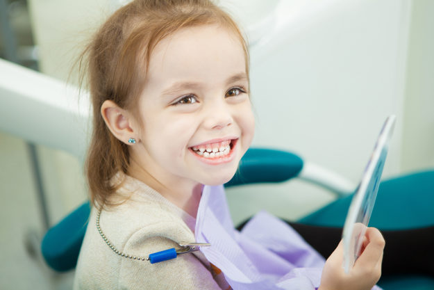 when should a child go to the dentist (3) child smiling at dentists after mom asked When Should A Child Go To The Dentist